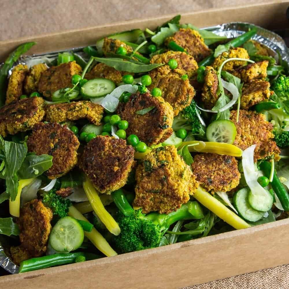 Vegetarian falafel with fresh vegetables and greens on a wooden tray.