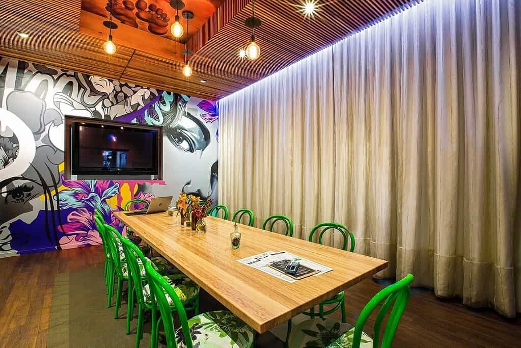 Contemporary meeting room with vibrant mural, wooden ceiling, and green chairs.