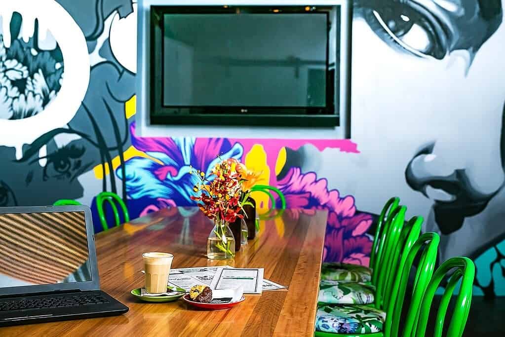 A table with a laptop and green chairs in front of a mural.