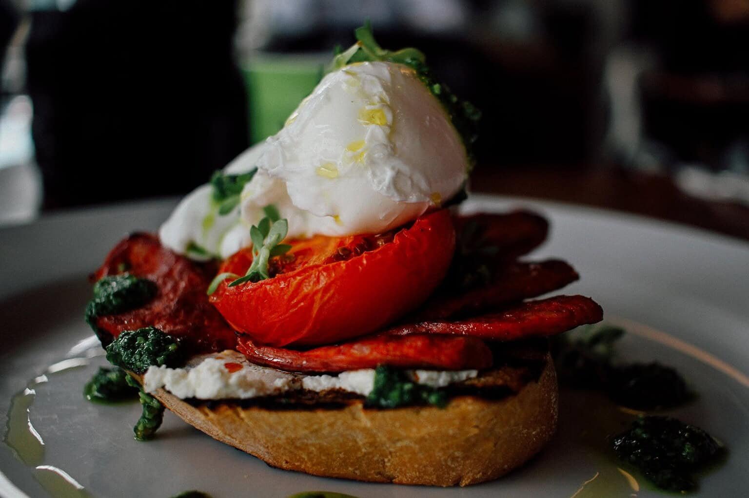 Delicious gourmet toast with poached egg, tomato, and greens on a white plate.
